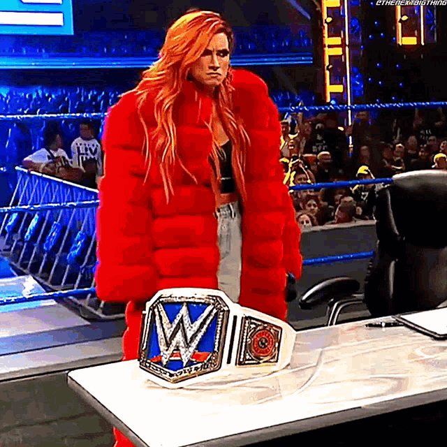 a woman in a red fur coat is standing next to a wrestling belt .