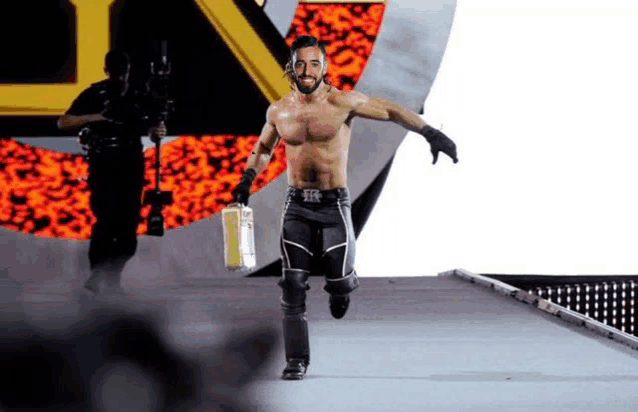 a wrestler without a shirt is walking down a ramp holding a briefcase .
