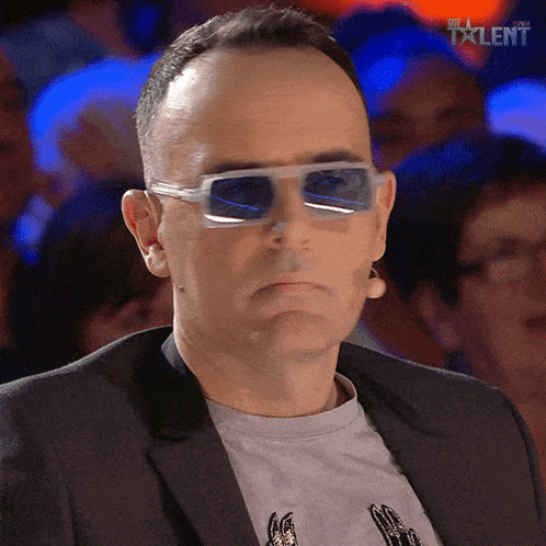a man wearing sunglasses and a suit is sitting in front of a crowd with the word talent on the bottom right