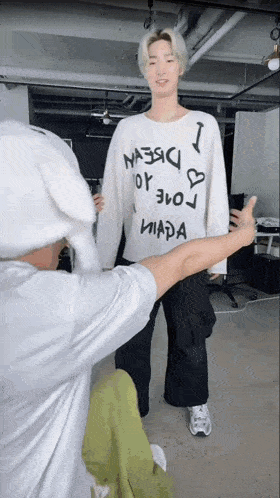 a man is giving a thumbs up while standing next to another man wearing a white sweater with graffiti on it .