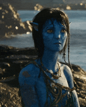 a woman with a blue face and yellow eyes is sitting on a rock near a body of water