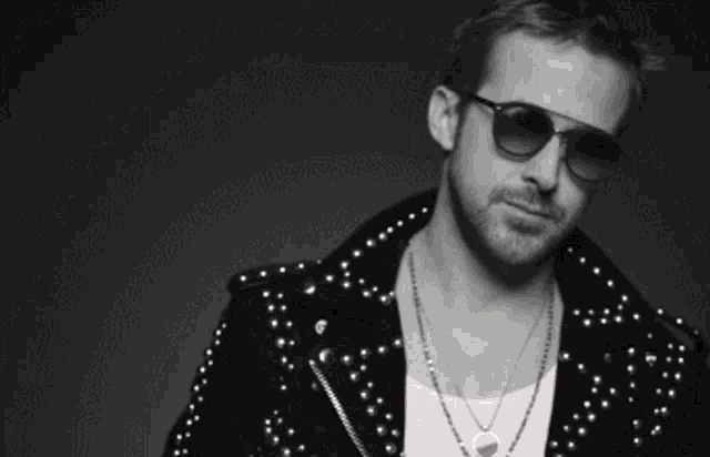 a black and white photo of a man wearing sunglasses and a studded jacket