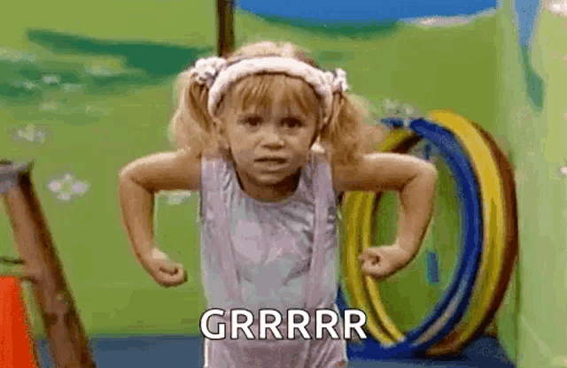 a little girl is doing push ups in a gym with a hula hoop in the background .