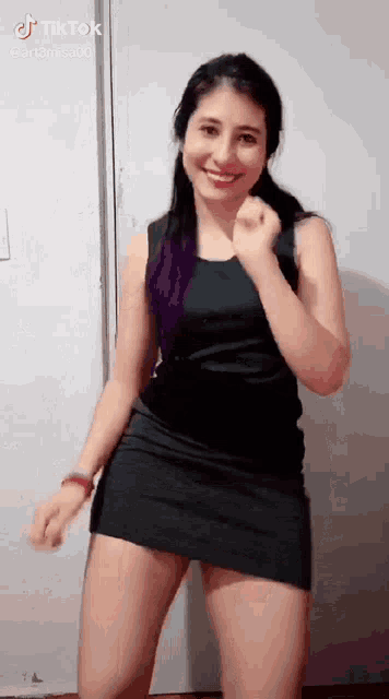 a woman in a black dress is dancing in front of a door and smiling .