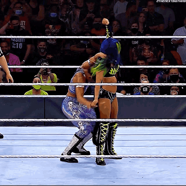 a woman with green hair is wrestling another woman in a ring with a crowd watching