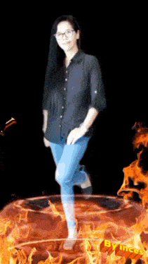a woman in a black shirt and blue jeans is standing in a circle of flames