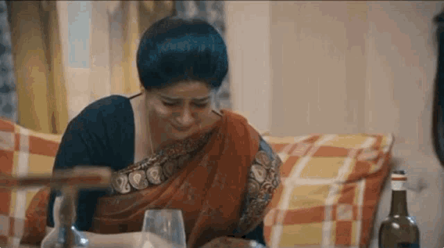 a woman in a sari is crying while sitting at a table .