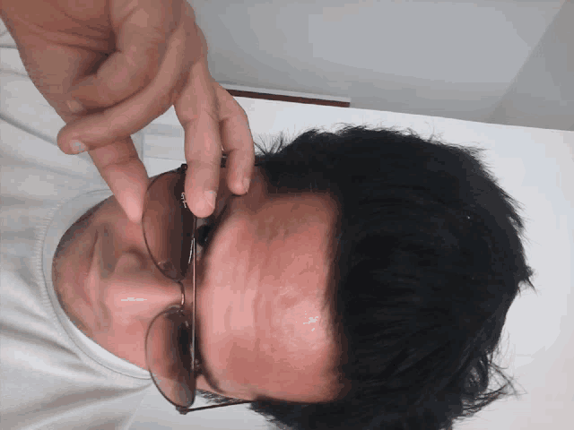 a man wearing sunglasses and a white shirt has his hand on his face