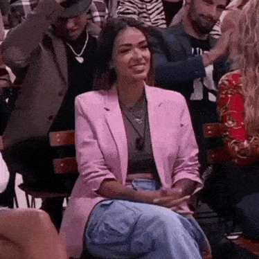 a woman is sitting in a crowd of people wearing a pink jacket .