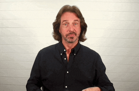 a man with long hair and a beard is wearing a black shirt with white buttons
