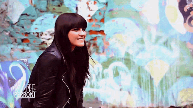 a woman in a black leather jacket is smiling in front of a wall with the word perront written on it