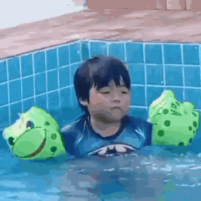 a young boy is swimming in a pool with frog floaties on his arms