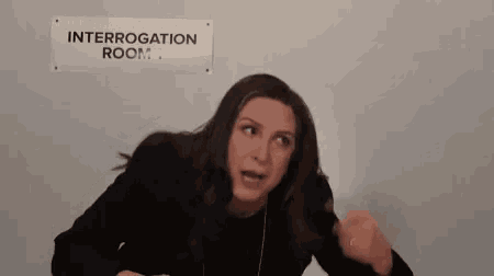 a woman is sitting in a interrogation room with a sign on the wall .