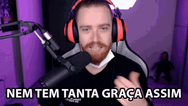 a man wearing headphones and a mask is sitting in front of a microphone with the words nem tem tanta graça assim above him