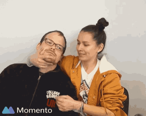 a woman is holding a man 's neck while wearing a college medicine shirt