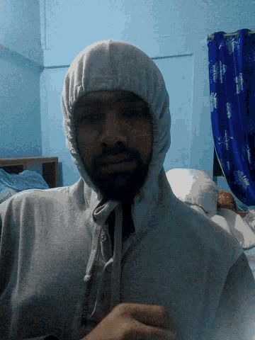 a man wearing a hooded sweatshirt with a blue curtain behind him