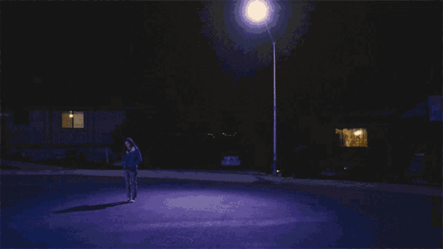 a person standing on a street at night with a street light in the background
