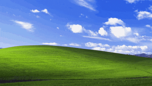 a lush green hillside with a blue sky and white clouds