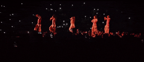 a group of women are dancing in a dark room with their hands in the air