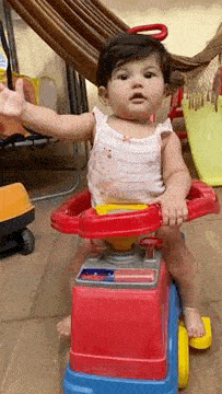 a baby girl is sitting on a red and blue toy car .