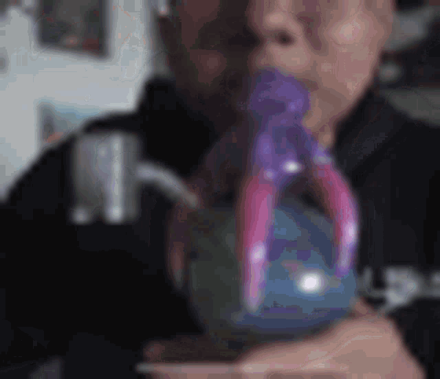 a man is blowing a purple balloon into a glass .