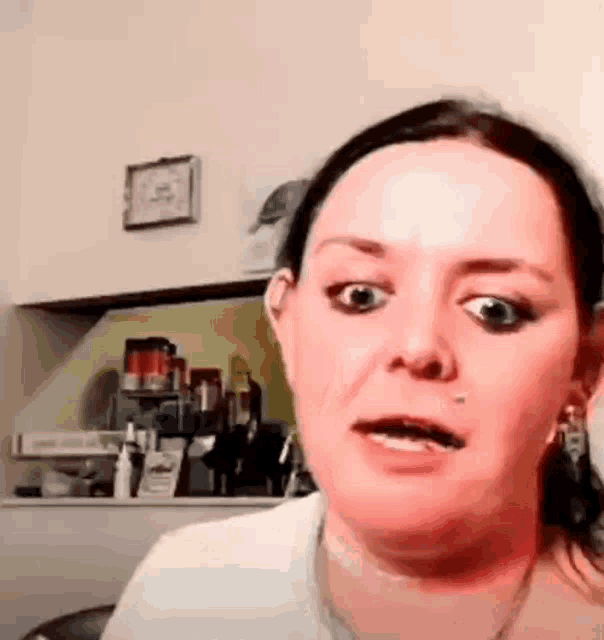 a woman is making a funny face in a kitchen with a clock on the wall .