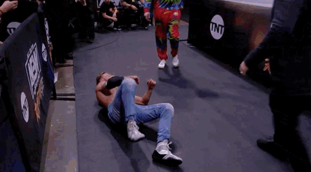 a man in a tie dye shirt is laying on the ground in a wrestling ring