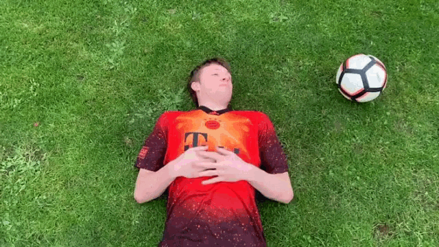 a man laying on the grass with a soccer ball in the background