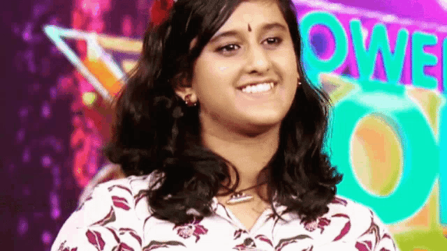 a young girl is smiling in front of a colorful background and looking at the camera .