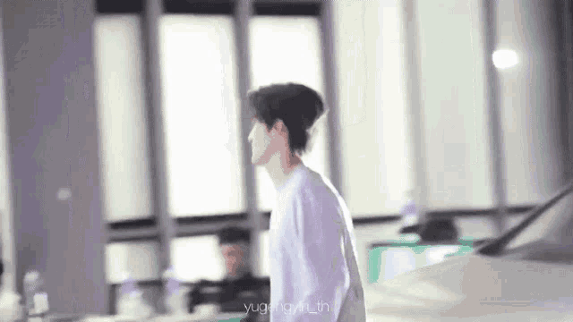a man in a white shirt is walking in a room with a car in the background .