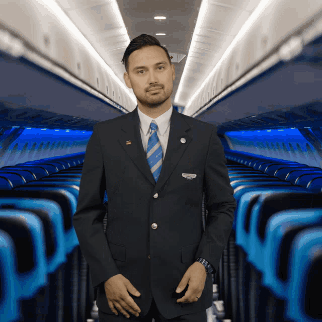 a man in a suit and tie stands in an airplane aisle