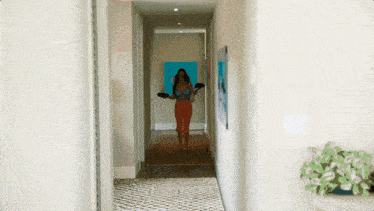 a woman walking down a hallway with a blue painting on the wall behind her