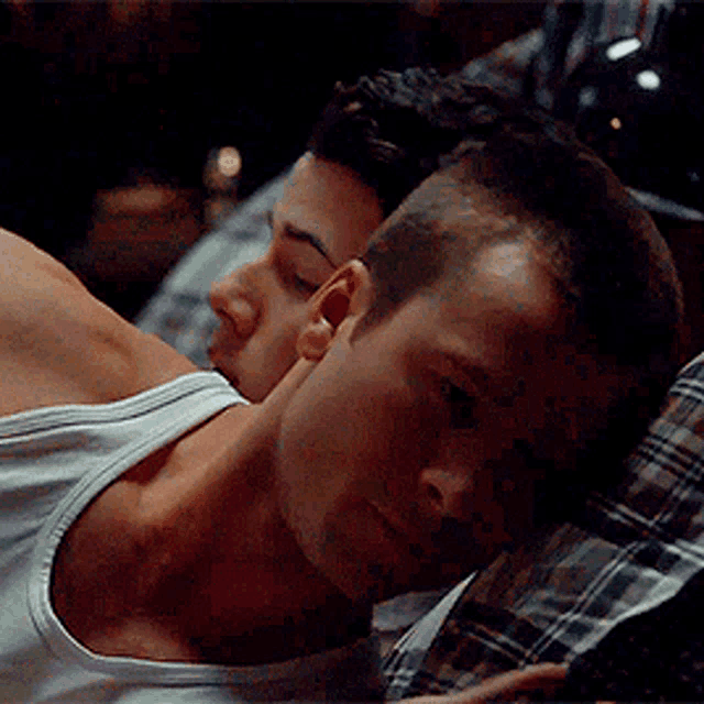 a man in a white tank top is laying on another man 's chest