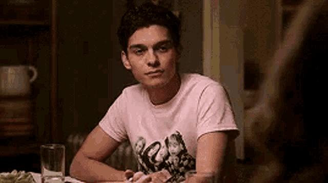 a man in a pink shirt is sitting at a table with a glass of water .