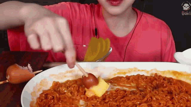 a person in a red shirt is eating noodles and cheese with a toothpick