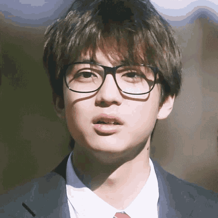 a young man wearing glasses and a suit and tie .