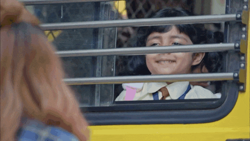 a little girl smiles while looking out of a yellow bus window