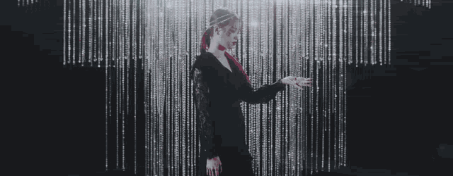 a woman in a black dress stands in front of a curtain of rhinestones