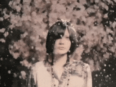 a woman is standing in front of a tree with flowers falling on her face .