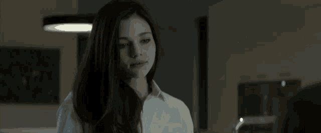 a woman with long dark hair is wearing a white shirt and looking at something
