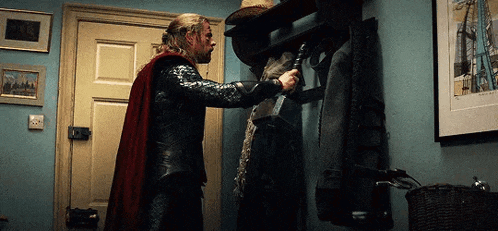 a man in a superhero costume is standing in a hallway holding a sword .