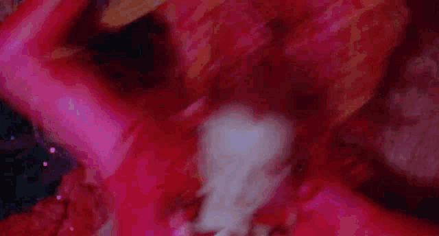 a woman with red hair and pink makeup is laying on a red surface .