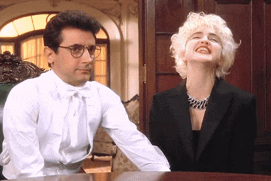a man and a woman are sitting at a table and the woman is wearing a wig
