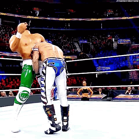 two men are wrestling in a wrestling ring with a woman watching .