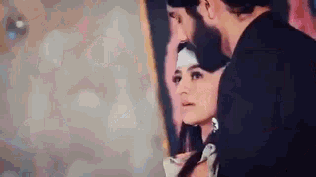 a man and a woman are standing next to each other in a room . the woman has a bandage on her head .