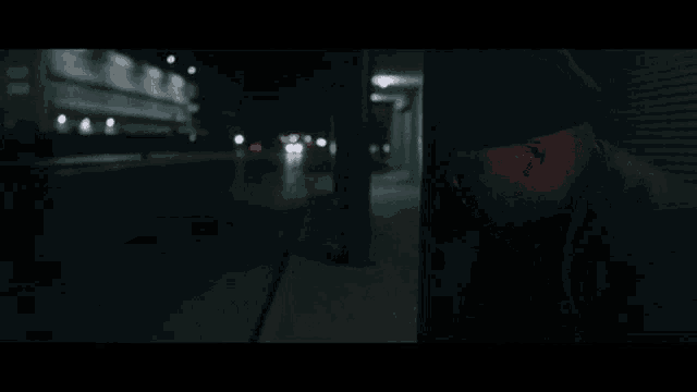 a man in a black hat is leaning against a wall in a dark alleyway .