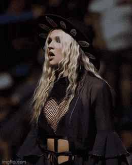 a blonde woman wearing a black hat and a black top is standing in front of a crowd ..