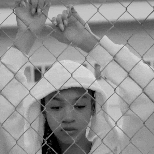 a girl behind a chain link fence wearing a hoodie