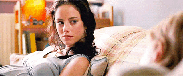 a woman is sitting on a couch with a pillow on her chest looking at the camera .