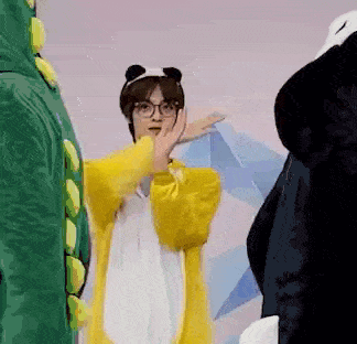 a person wearing a yellow jacket and a panda costume is standing next to a green dinosaur costume .